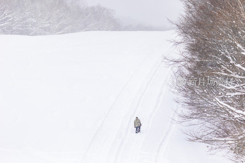 一个人带着滑雪板爬上雪山