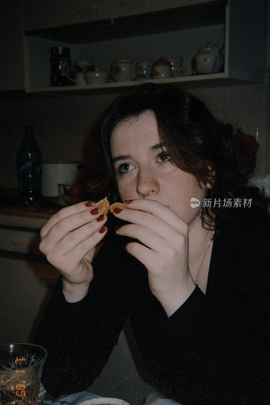 年轻的女人正坐在桌旁吃橘子。的照片