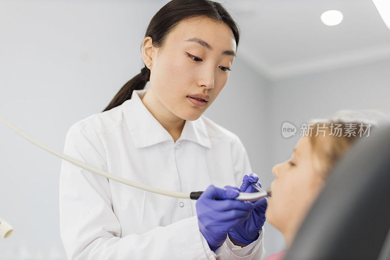 儿童亚洲女牙医治疗牙齿的女孩，使用牙钻和镜子。