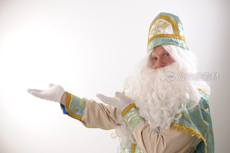 白色的胡子和圣尼古拉斯的两只手的金蓝色西装指向白色背景上的“美国”文本广告的空余空间。荷兰圣诞老人圣尼古拉斯圣诞新年