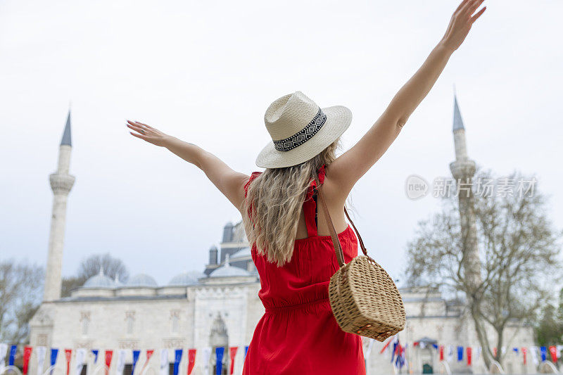 一位美丽的旅游博主女孩身穿红色长裙，头戴草帽，在土耳其伊斯坦布尔的古代景点拍照