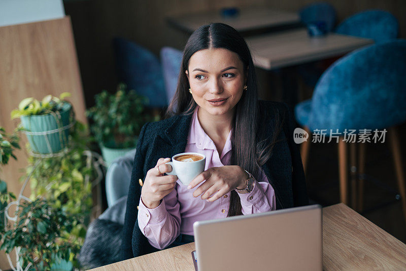 一个漂亮的年轻女人拿着笔记本电脑和一杯咖啡坐在咖啡馆里