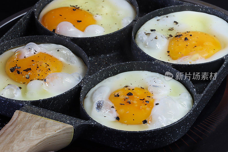 全画幅的不粘锅与煎蛋环，四个鸡蛋正在烹饪锅上的陶瓷滚刀，高架视图，重点在前景