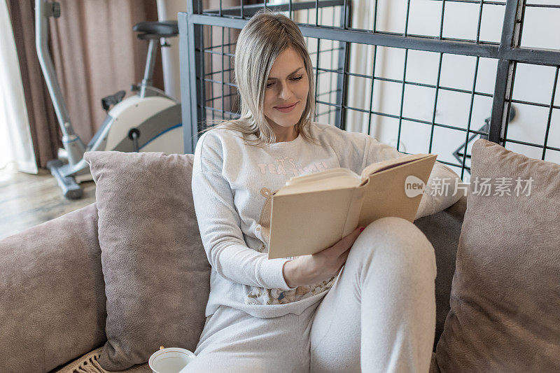 读一本好书，早上喝杯咖啡。穿着睡衣的女人正在家里看书。