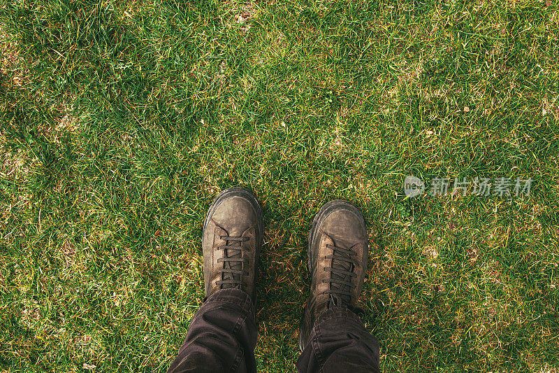 穿着靴子的男性脚站在绿色草坪上的俯视图