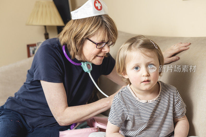 祖母和孙女扮演医生和护士，祖母用玩具听诊器检查孙女的背部