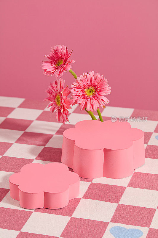高角度拍摄的两个基座在花朵形状显示在粉红色方格桌布与地板非洲菊装饰。垂直照片用于促销，空白空间用于展示产品