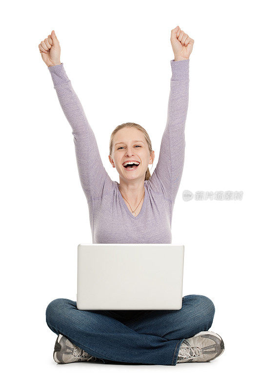 快乐的年轻女子举起手臂，膝上放着笔记本电脑