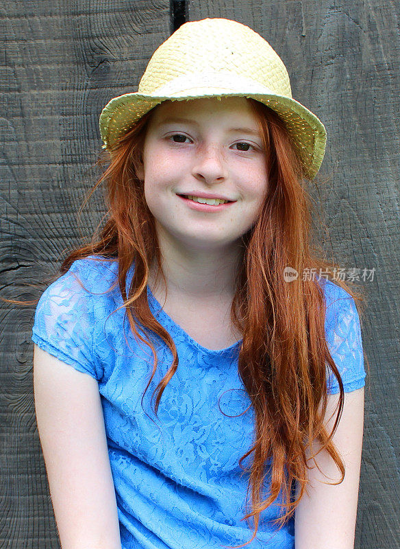 女孩坐在花园里，木制的背景，长长的红头发，帽子，蓝色的衣服