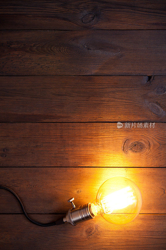 老式的白炽灯爱迪生式灯泡在旧木桌上