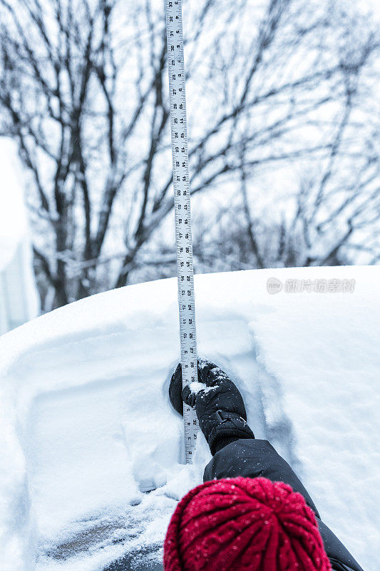 一名妇女伸手测量汽车顶上的积雪