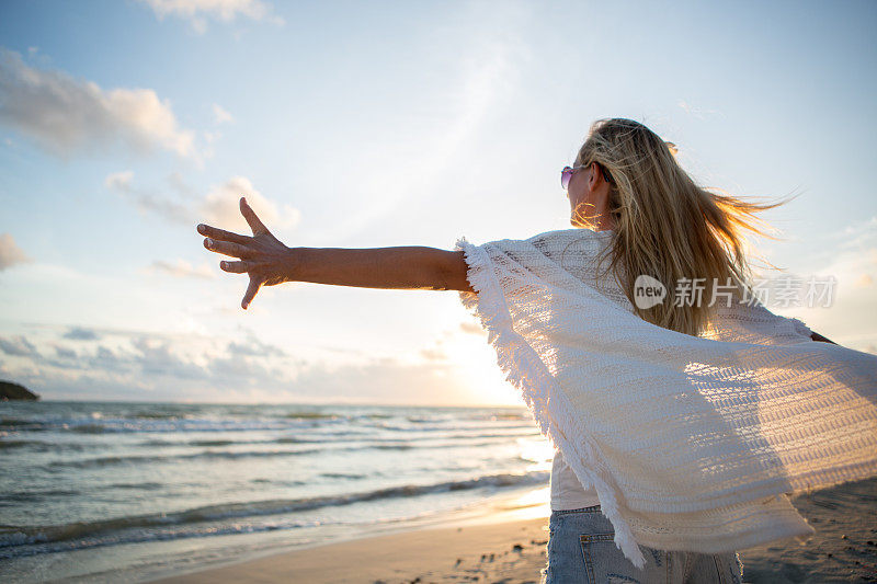 放松的女人呼吸着新鲜空气，在日落举起手臂