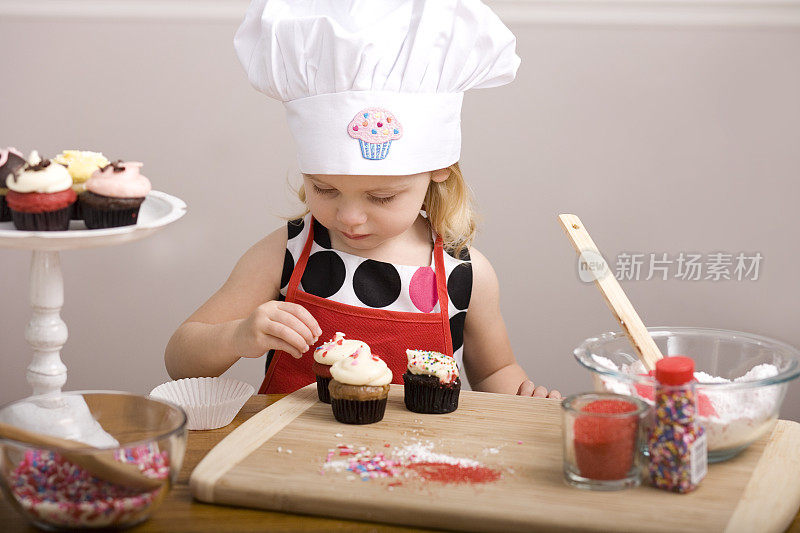 小女孩戴着厨师帽和围裙装饰纸杯蛋糕