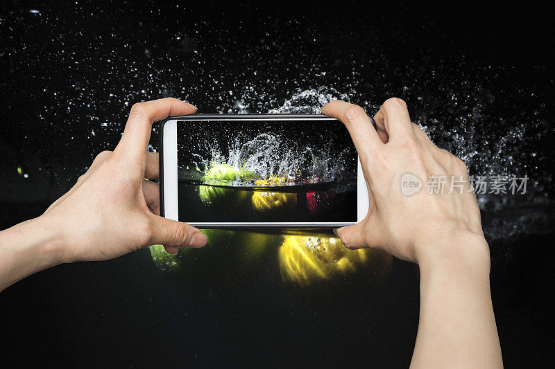 用智能手机拍照，把水果泼到水里。黑色背景的新鲜水果