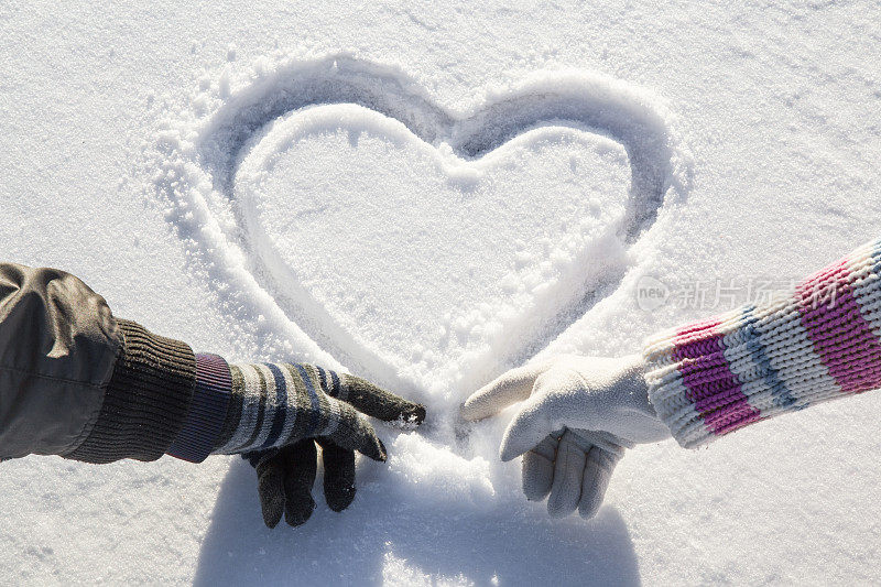 双手在手套里在湖面上的雪地上画出心形。阳光灿烂的冬日。男人和女人。情人节的概念。