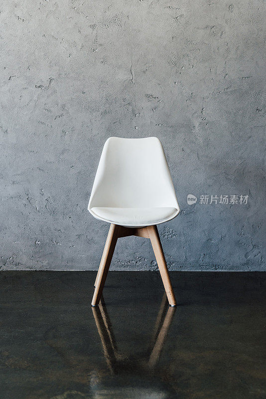 在极简主义风格的灰色墙壁附近的空现代白色椅子