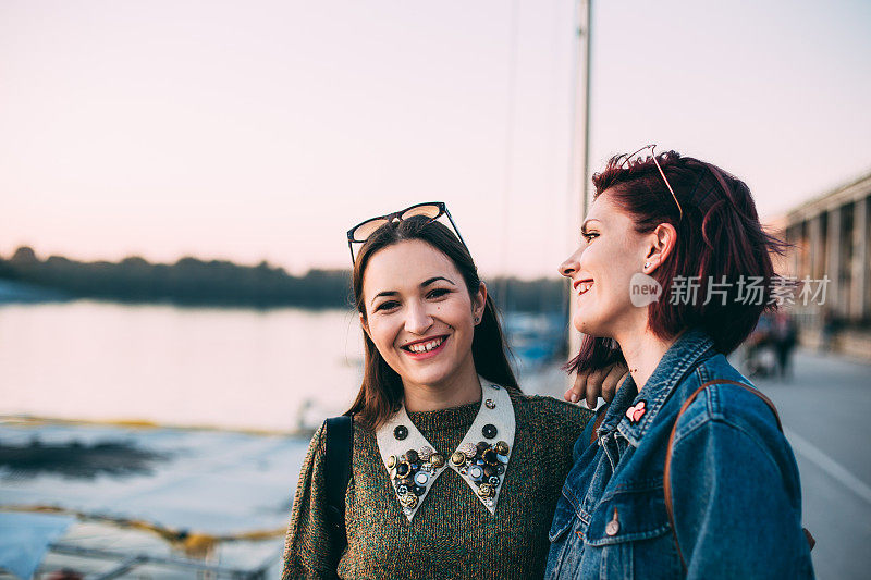 美丽的年轻女孩沿着河边的码头散步，一边聊天，一边拍照