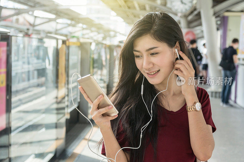亚洲女性乘客穿休闲装使用和听歌曲通过智能手机在轻轨或地铁在大城市旅行，生活方式和交通理念