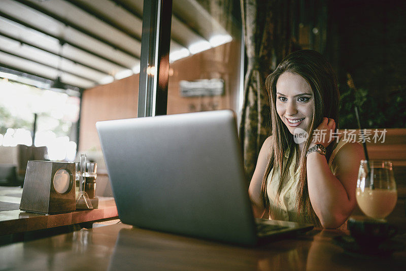 可爱的女性在餐厅喝果汁的时候用笔记本电脑购物