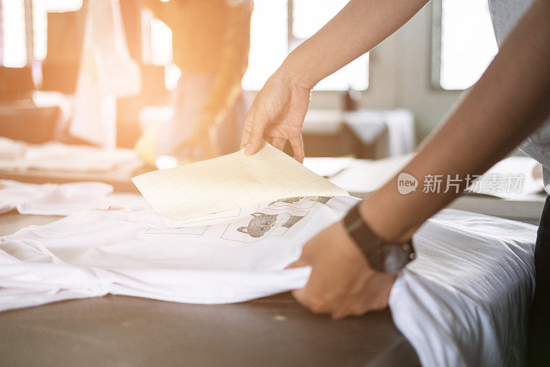一名年轻女子在商店里从织物上的防水薄膜中抽出一张纸。手工丝印t恤的工人。