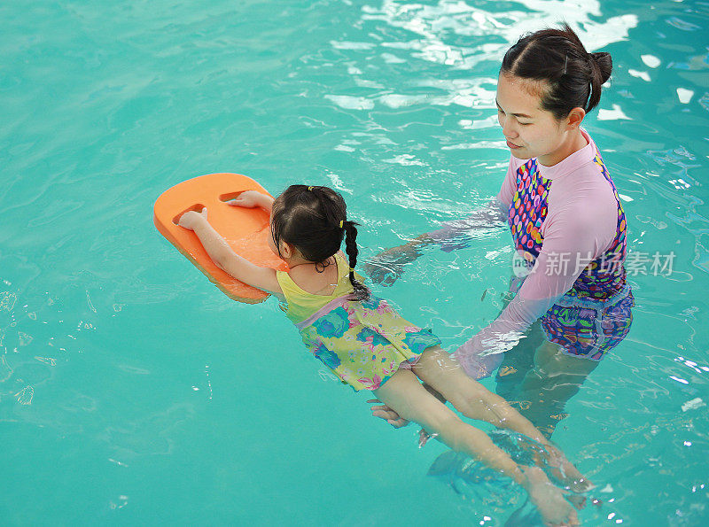 妈妈和孩子在游泳池里游泳。快乐的年轻女子教她的女儿游泳。