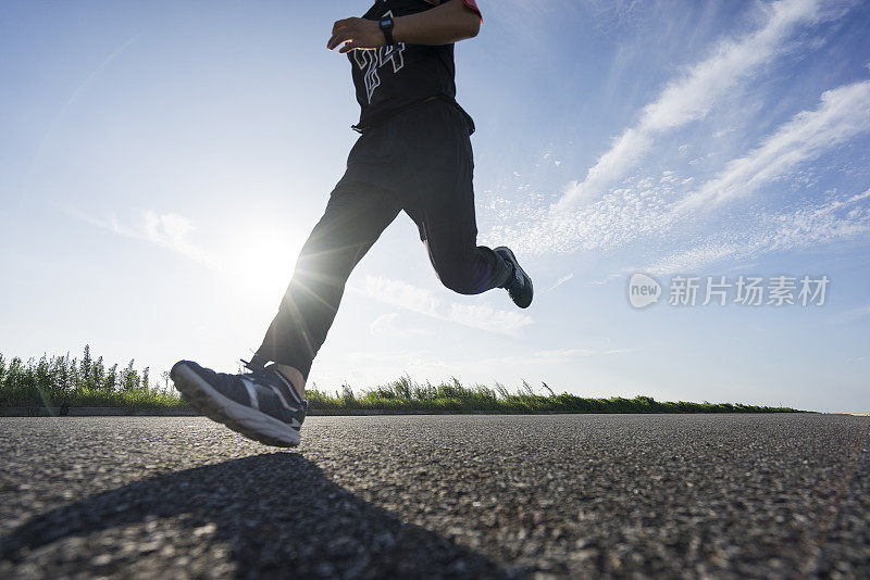 年轻的男运动员在柏油路上迎着天空奔跑