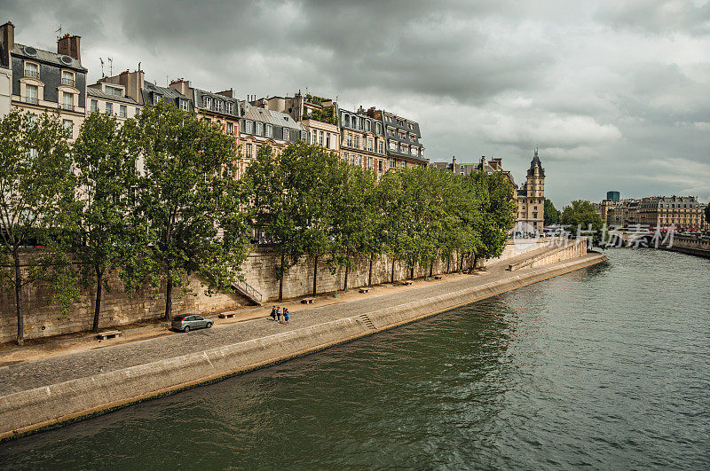 阳光普照的巴黎塞纳河岸边，古老的建筑、长廊和成行的树木。