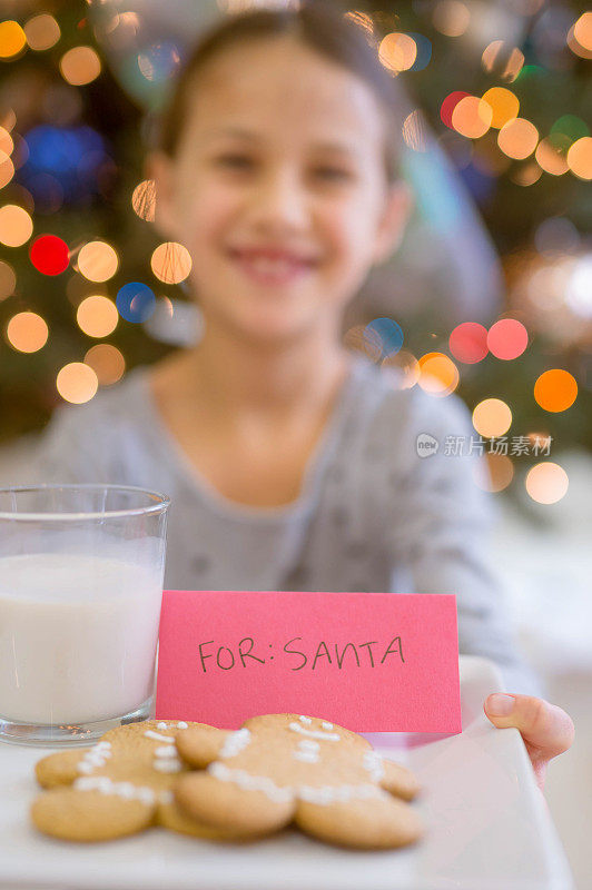 一个小女孩端着一盘饼干和牛奶给圣诞老人