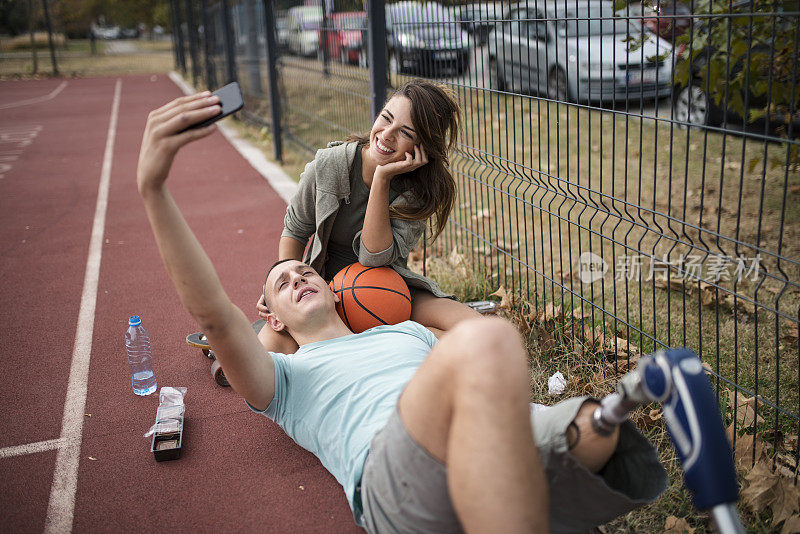 一对年轻情侣躺在篮球场上自拍