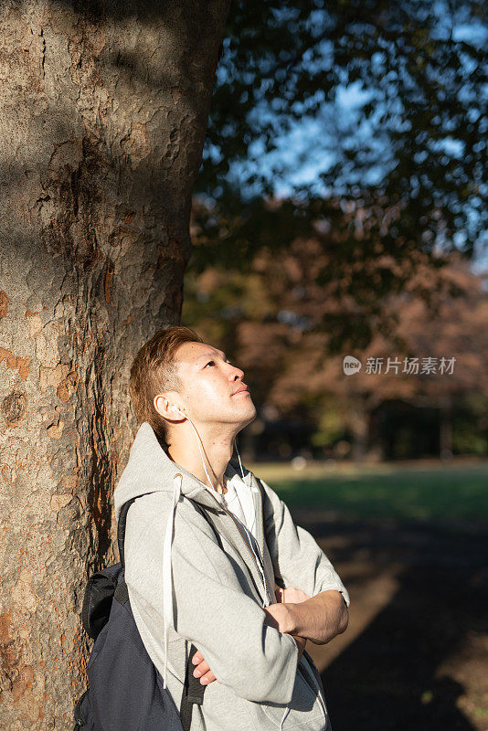 年轻人靠在树上，戴着耳机听音乐