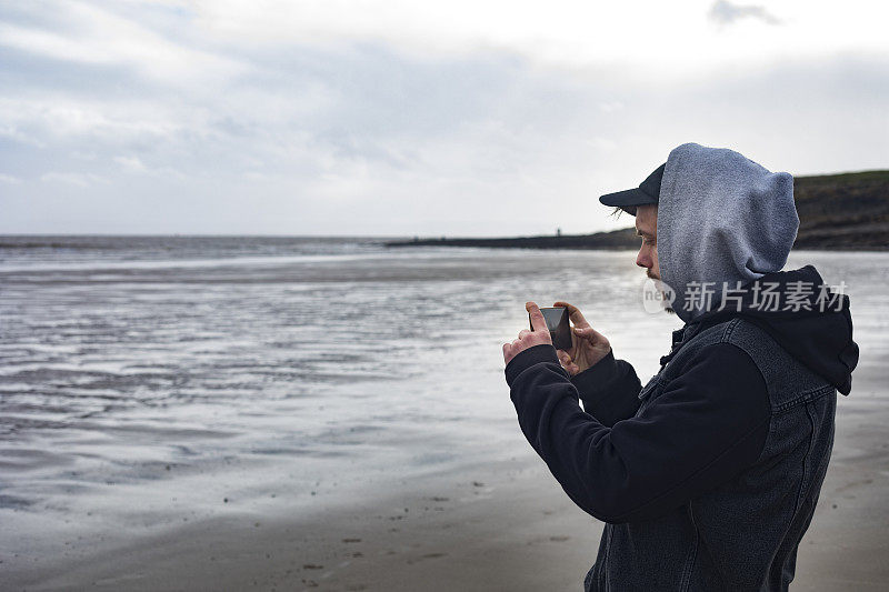 年轻的成年男子在海滩上用手机拍照