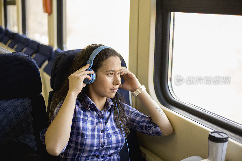 享受乘火车旅行。年轻女子戴着耳机听音乐，喝着咖啡