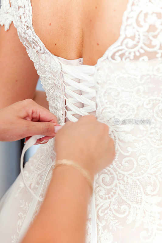 伴娘在婚礼前帮助新娘系好她的白色婚纱