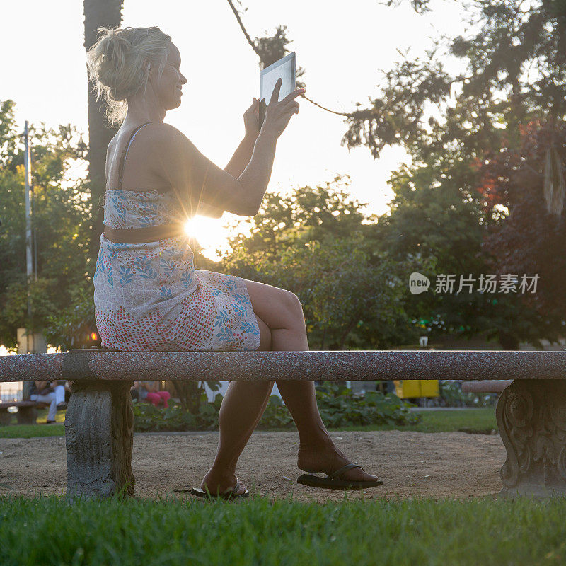 日出时分，一名成熟女子在公园里使用平板电脑