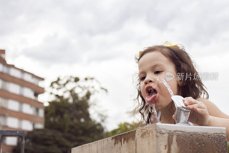 一个拉丁女孩边喝边玩喷水。