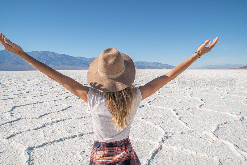 年轻女子张开双臂站在沙漠的盐滩上，凝视着壮观的风景;女孩旅行，发现世界