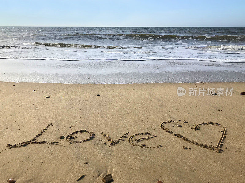 图片写在阳光沙滩上用爱的词和在沙子上用棍子画的心，由海浪，概念社交媒体照片手写字母在柔软的黄金沙滩上，多塞特，英国海边的海岸线