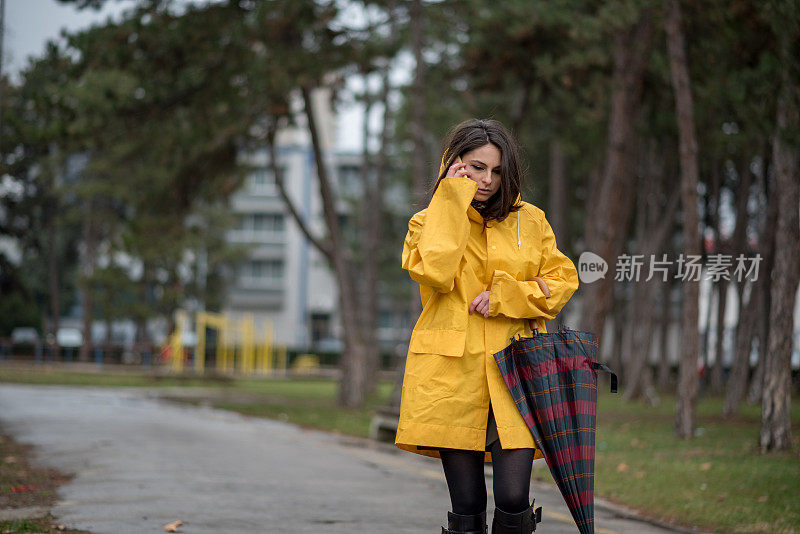 穿着黄色雨衣的年轻女子在公园里度过雨天