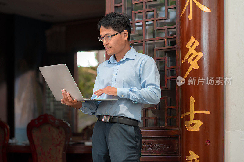 中国商人站在传统中式房间前看电脑