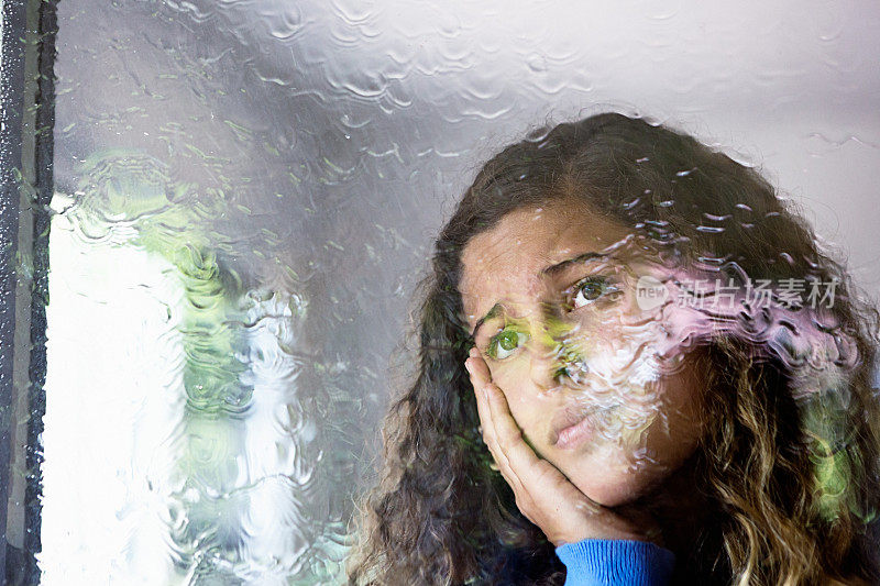 年轻寂寞的女人望着她的雨中的城市窗口