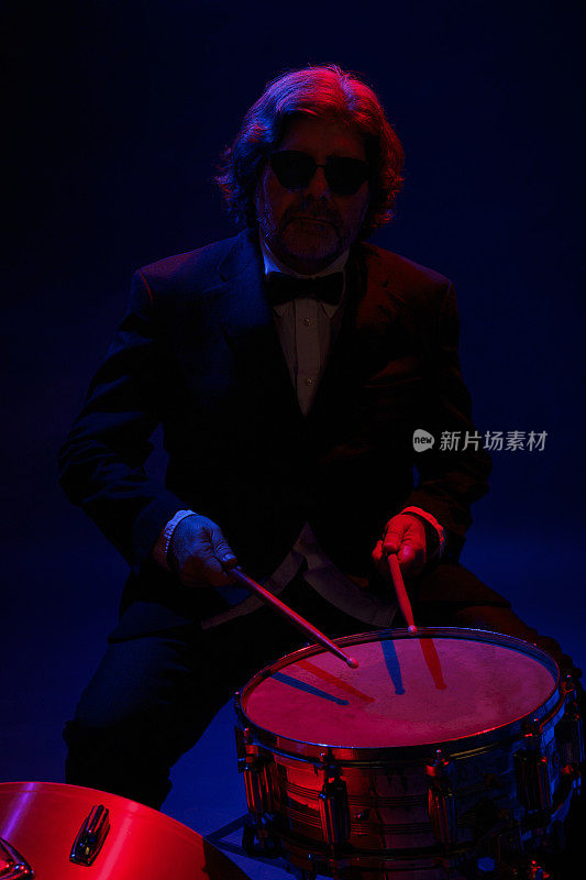 音乐家鼓手活跃的高级英俊男子打架子鼓。蓝色背景，光线和烟雾特效。