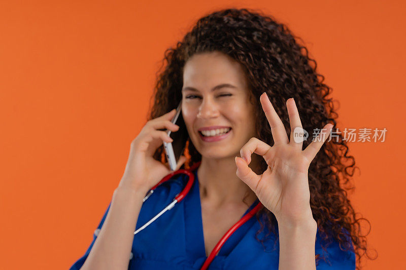 年轻女医生使用智能手机，显示ОК标志，橙色背景