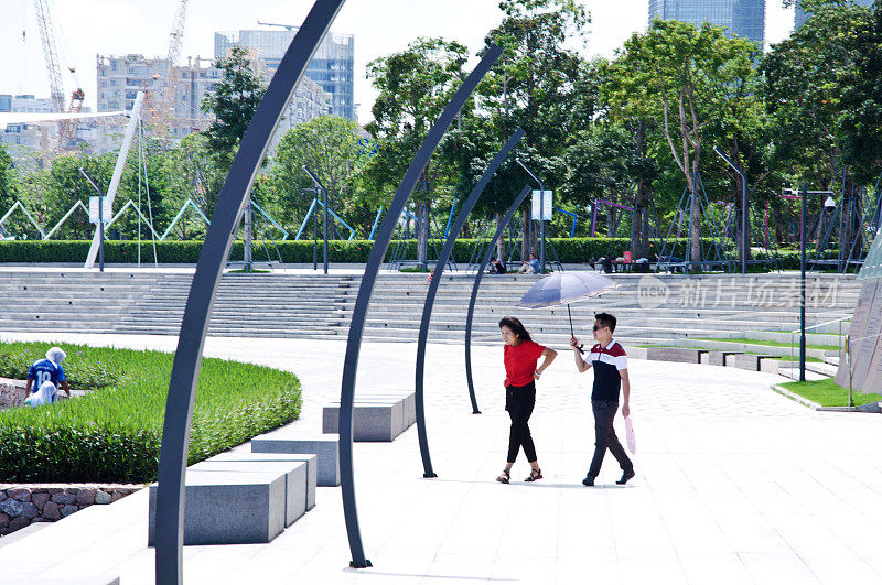 在中国深圳的深圳人才园，一对夫妇正在用雨伞遮挡烈日。这个公共主题公园与深圳湾公园和湾体育馆相连