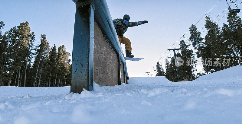 一个滑雪板在完整的冬季装备骑特技轨道与森林和滑雪跳跃在背景在埃尔多拉滑雪度假村附近博尔德，科罗拉多州在一个光明，阳光，冬日