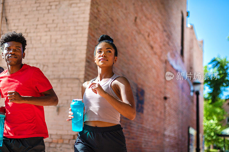 千禧年男性和Z一代女性在炎热的夏日里锻炼，拿着水瓶补水