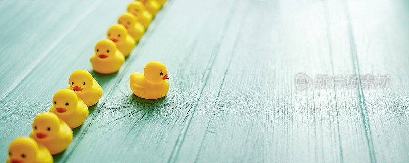 一排正式的黄色橡胶鸭子，其中一只鸭子脱离了线，沿着自己的方向，场景设置在一个古老的绿松石色风化木面板背景上，概念上代表水。