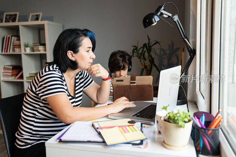 亚洲母亲在家用笔记本电脑工作，儿子在用数码平板电脑