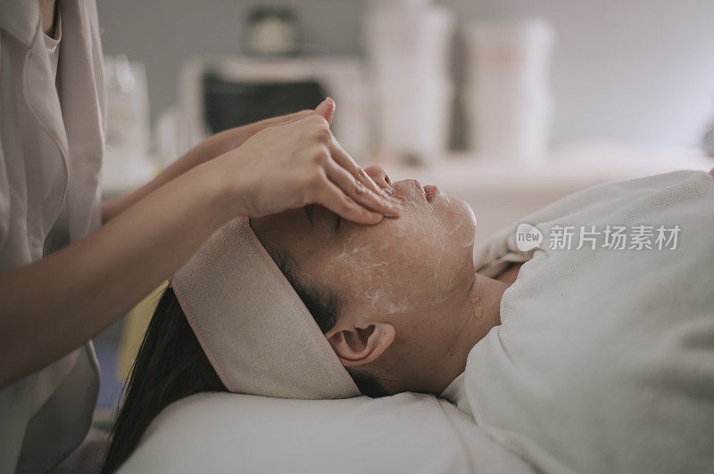 亚洲华人女性美容师清洁擦拭做面部治疗，为她的客户在面部美容沙龙