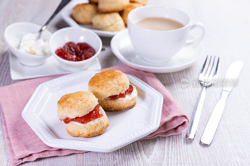 英式英式司康饼加奶油和果酱，配上一杯茶放在白色的桌子上。