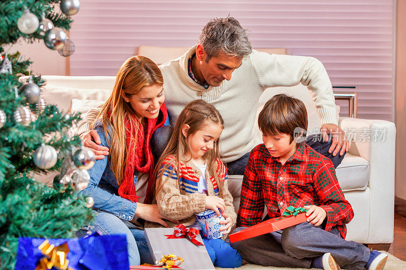 12月假期。圣诞节,甜蜜的时刻。圣诞节那天，一家人坐在圣诞树前的地毯上拆礼物